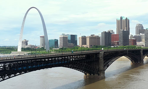 MetroLink train crossing Eads Bridge into St. Louis with the Arch and city skyline in the background