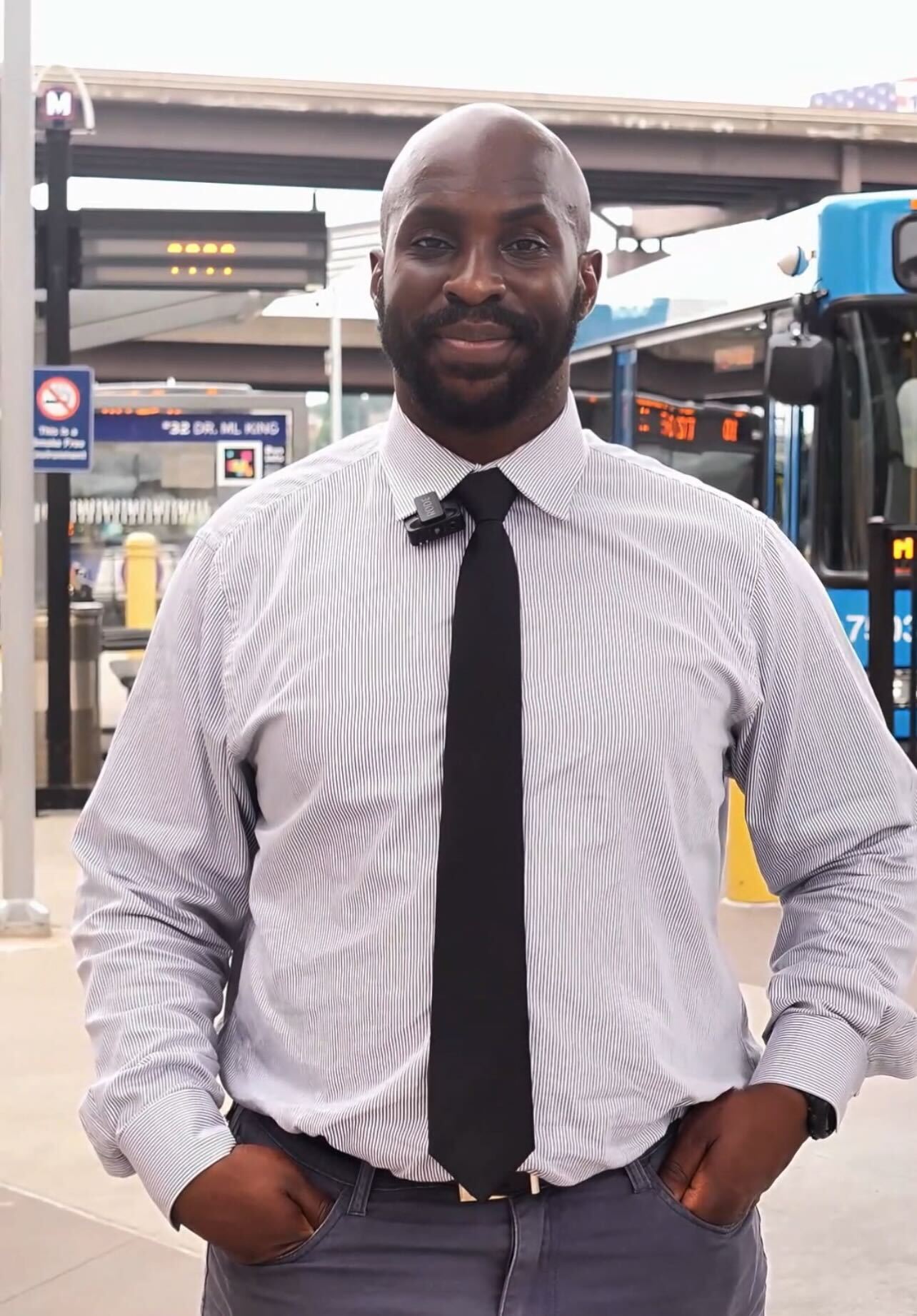 Chef Curtis, a successful Black man wearing a light-colored dress shirt and black tie, posing in front of a MetroBus